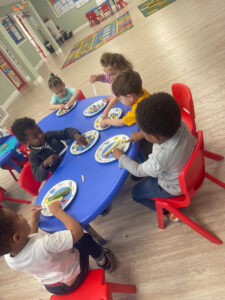Toddlers eating snacks around a blue table during classroom snack time.