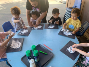 Preschool students sitting around a table engaging in hands-on shaving cream sensory activity at daycare.