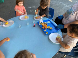 Children sitting around an outdoor table conducting a science experiment with lemons, color dye, vinegar, and baking soda.