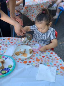 Toddlers sitting outside at a table eating finger foods during a tea time activity at daycare.