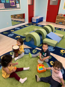 Toddlers sitting on a classroom carpet in a circle playing with kid-friendly musical instruments at daycare.