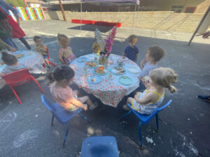 Toddlers sitting around an outdoor table eating snacks during snack time at preschool daycare.