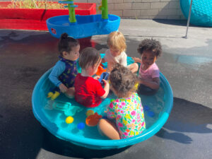 Toddlers playing together in a kiddie pool outside a preschool daycare.