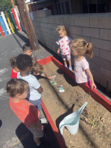 Children gathered around a garden ready to plant seeds during an outdoor activity.