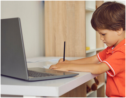 Preschool child working on an educational assignment with a laptop in front of him.