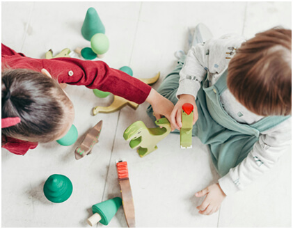 Top-down view of two toddlers playing together with toy dinosaurs at a daycare center.