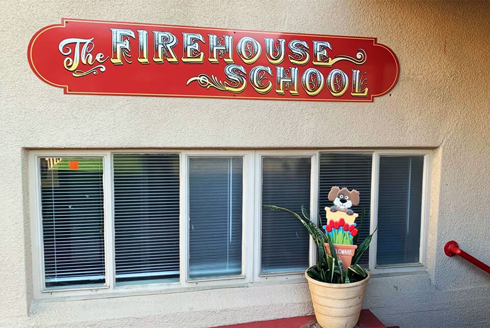 Exterior view of a preschool and daycare facility with a branded sign above the window that says "The Firehouse School."