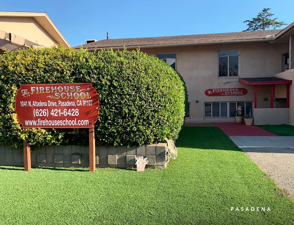 Front view of Firehouse School with perfectly mowed lawn, trimmed bushes, and an informational school sign.