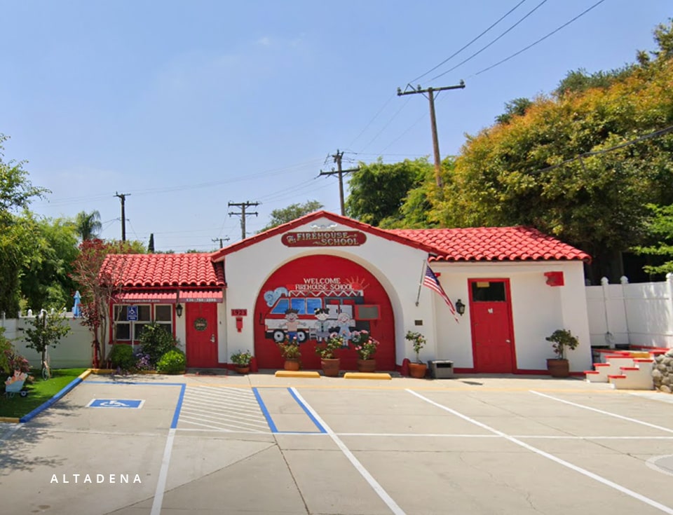 Front view of Firehouse School Altadena decorated with potted plants, featuring a red door and roof designed to resemble a realistic firehouse.