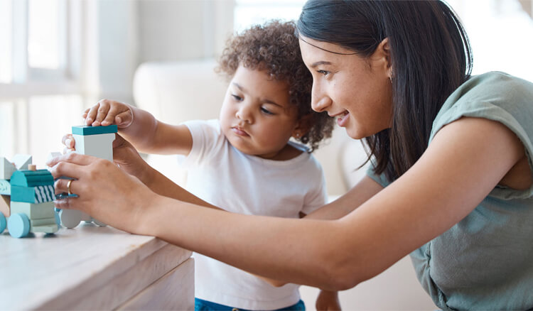 Caregiver playing and stacking blocks with a toddler, promoting fine motor skills and early learning.