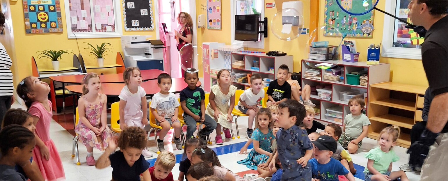 Guest performer demonstrating a bubble activity in front of a preschool classroom filled with engaged children.