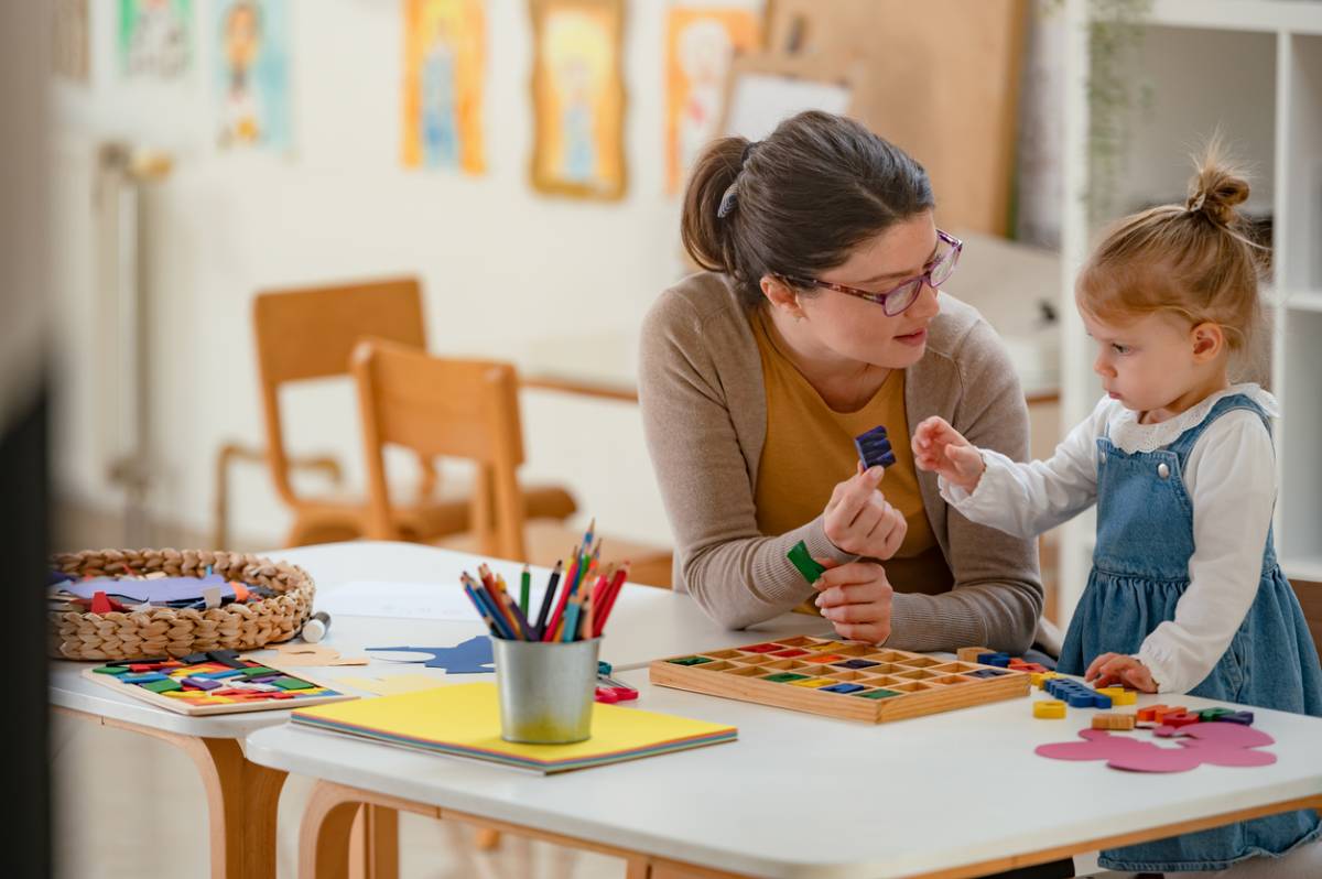 A young woman and a little girl engage in creative play with colorful building blocks in a bright classroom, fostering learning, fine motor skills, and early childhood development